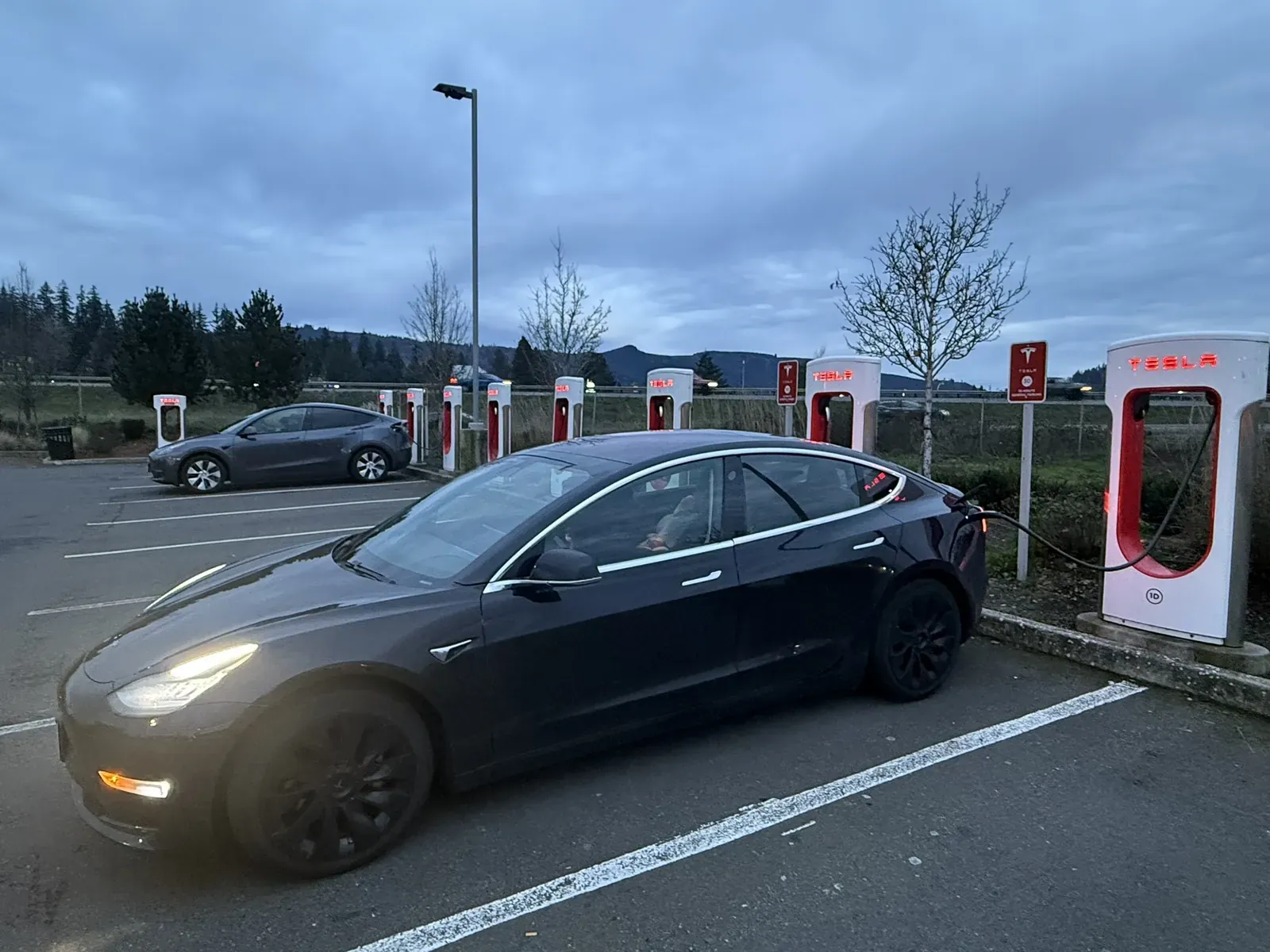 Black Model 3 parked at a Supercharger at dusk