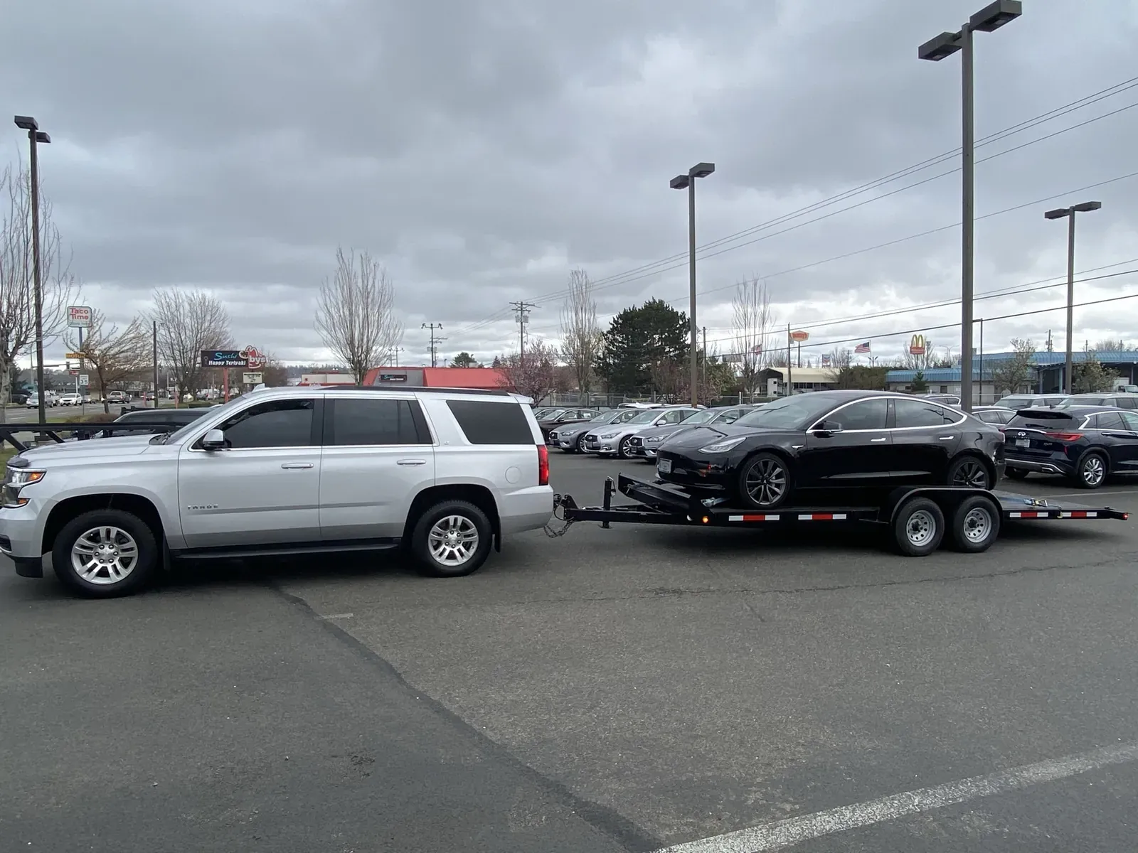Black Model 3 loaded on a flatbed car trailer behind an SUV
