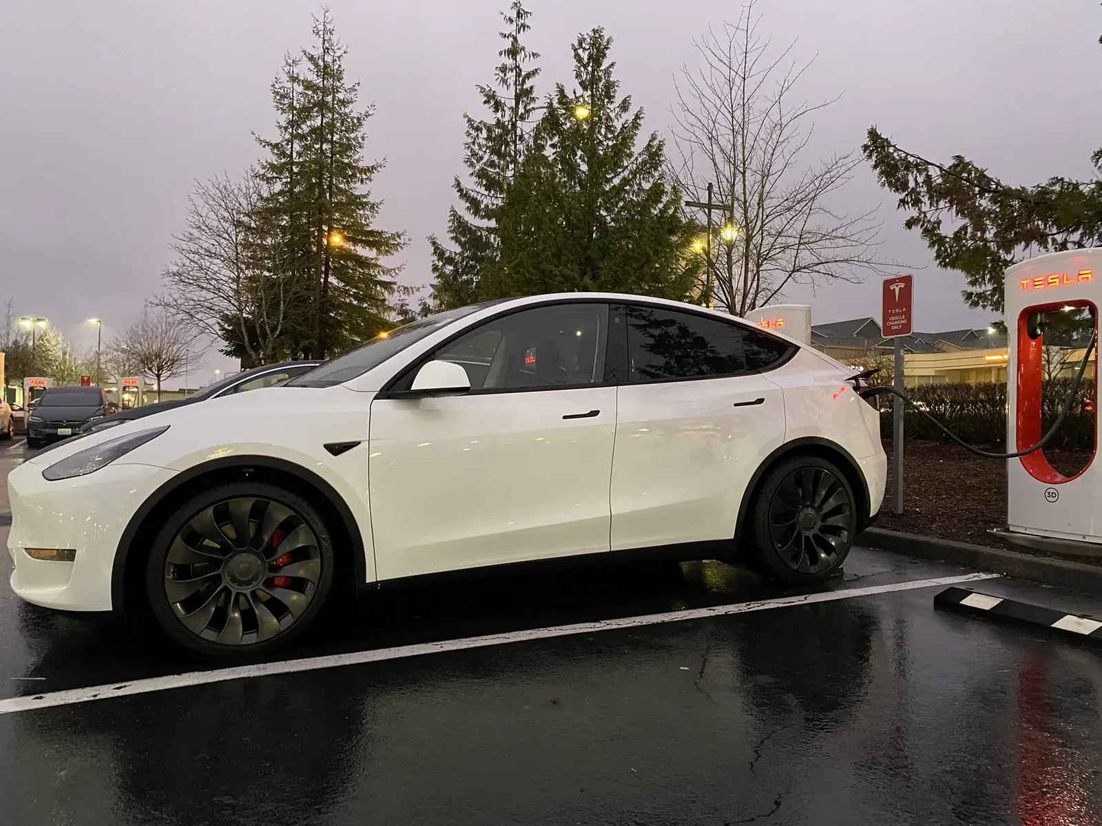 White Model Y Performance at a Supercharger in the evening rain