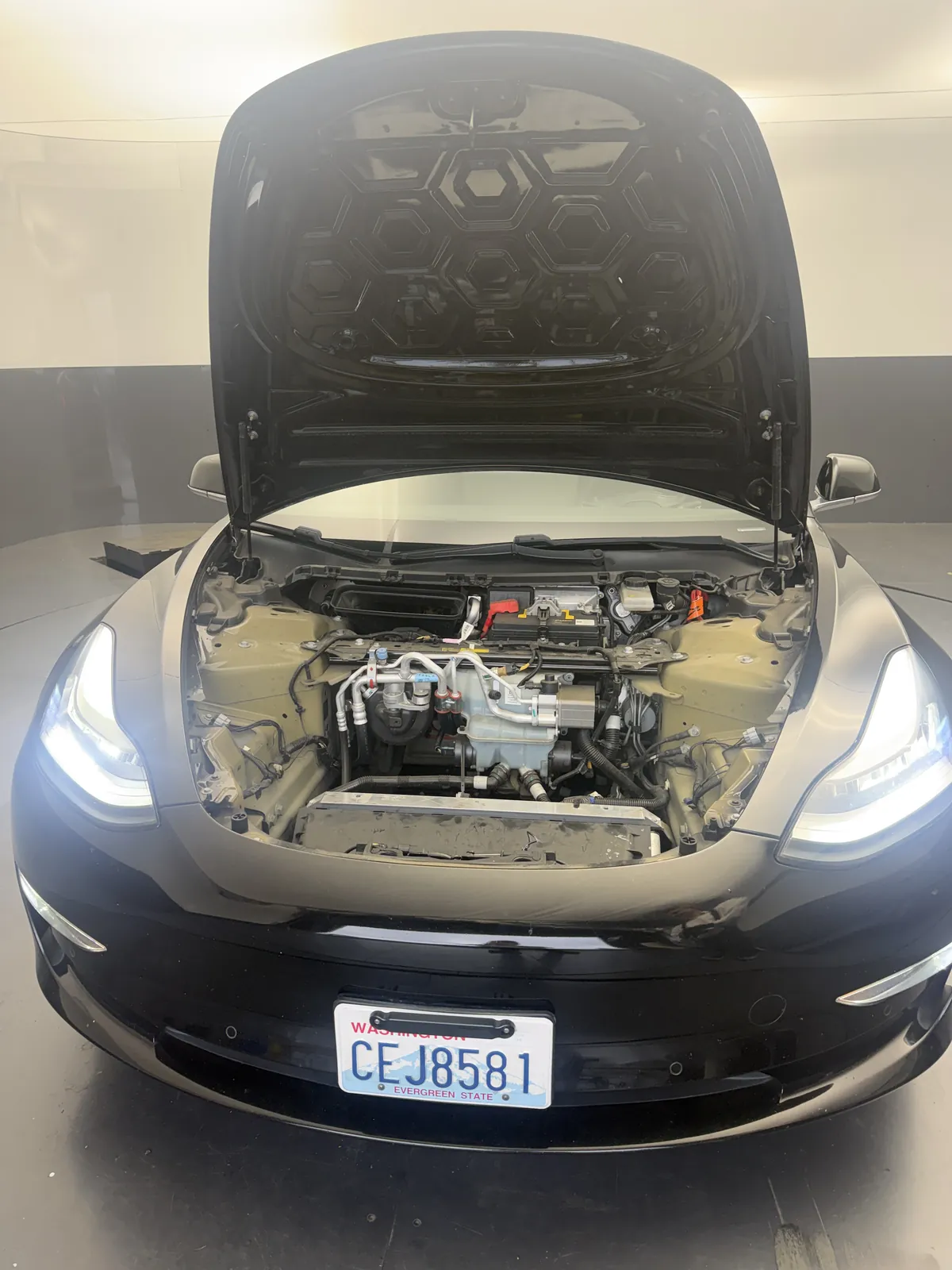 Black Model 3 with the hood up and the frunk tub removed, exposing the cooling components and the top of the radiator/condenser